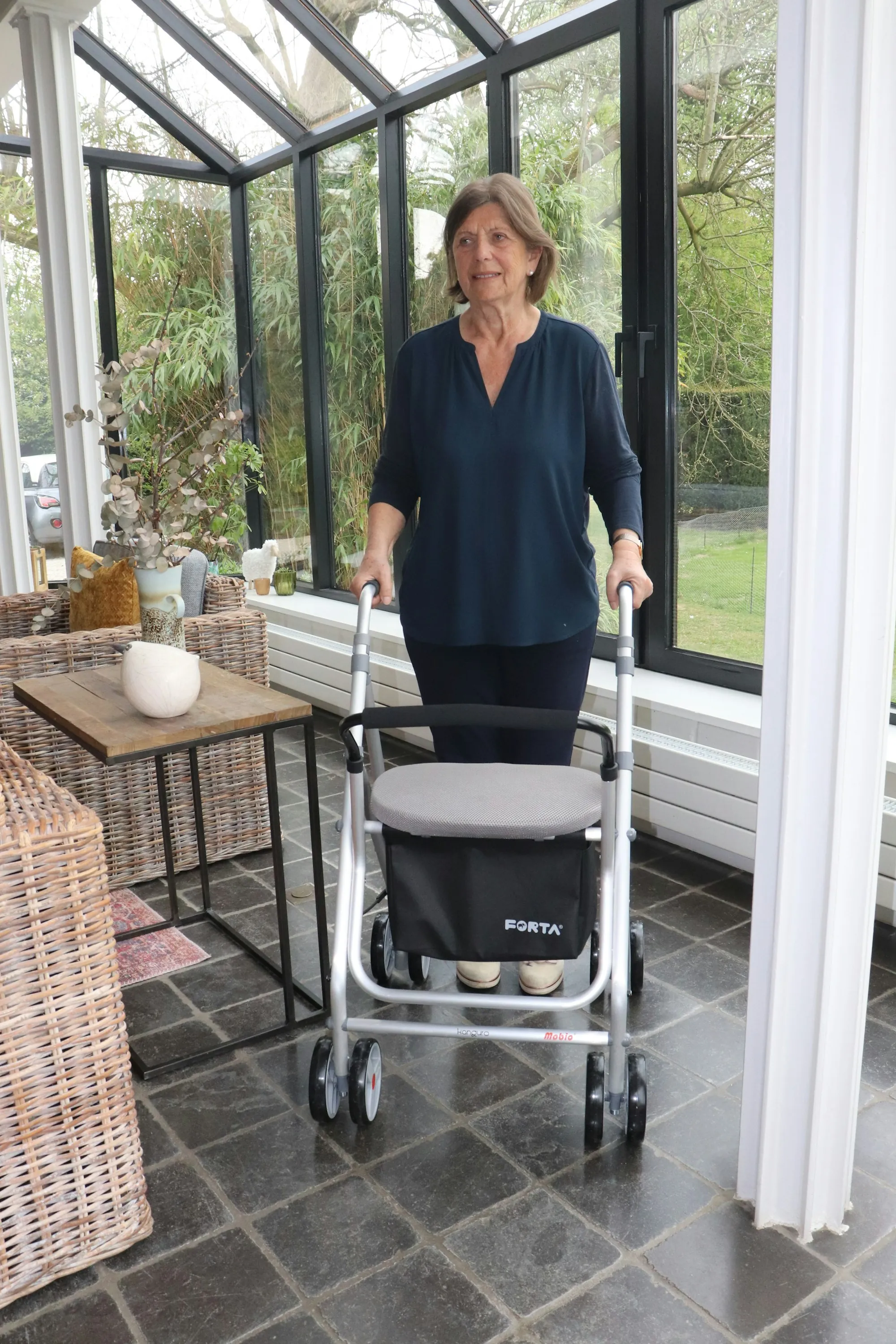 A woman using a walking frame in a bright sunroom